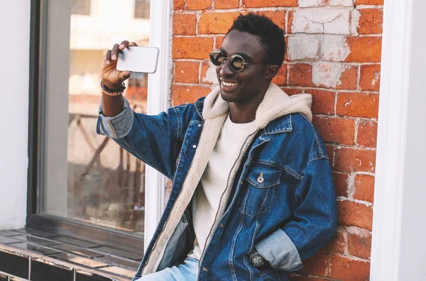 Mutlu gülümseyen Afrikalı genç bir adamın portresi. Şehir caddesinde akıllı telefonla selfie çekiyor.