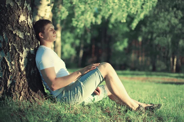 Töprengő ember ül egy fa közelében a szeme zárva, meditáció — Stock Fotó