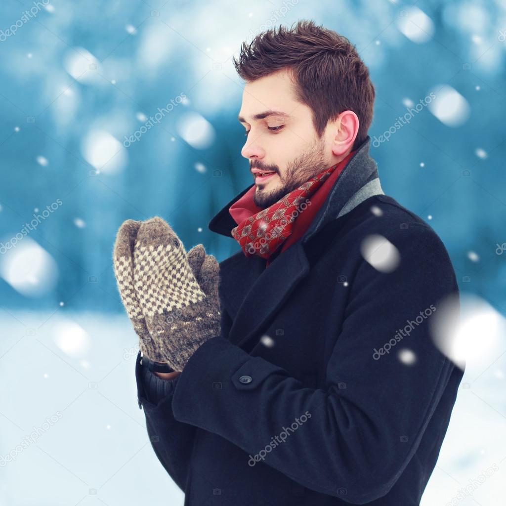 Handsome man in mittens freezes outdoors in winter snowy day 