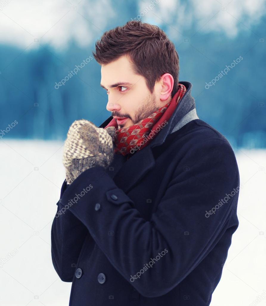 Handsome man in mittens freezes outdoors in winter cold day