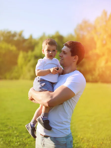 Retrato soleado de feliz padre joven sosteniendo a su pequeño hijo en las manos — Foto de Stock