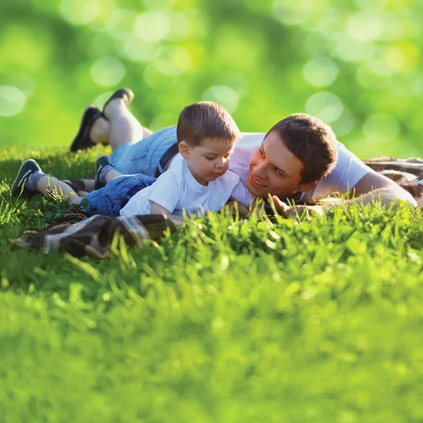Lato zdjęcie szczęśliwy ojciec i syn razem, leżącego na zielony świeży — Zdjęcie stockowe