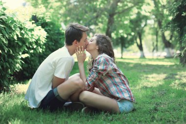Çimenlerin üzerinde oturan ve öpüşme aşık genç Çift 