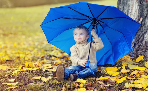Портрет симпатичного ребенка с пупсом, сидящего на желтых листьях — стоковое фото