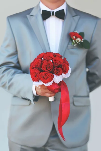 Beau marié tenant des fleurs de bouquet de mariage rouge — Photo