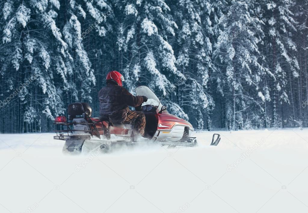 Driver man riding on a snowmobile through the snow in a snowy fo