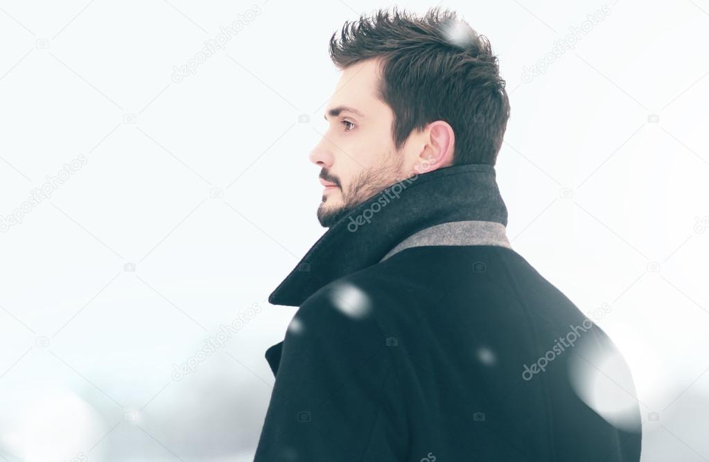 Portrait of fashion handsome man in winter snowstorm looks into 