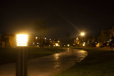 Gece parkında bir patika ve yanlarındaki çimenler boş. Birkaç lamba yanıyor.