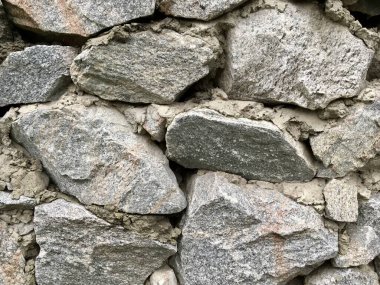 Kırsal taştan bir duvar. Havan mermisiyle bir arada tutulan sert kayalar sergileniyor. Taşlar soğuk açık gri tonlarda doğal hava ve doku karışımı sergiliyor. Yatay yakın plan fotoğraf..