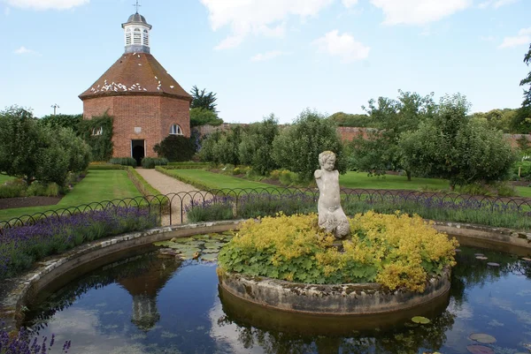 Gartenszene. alter Taubenschlag und Teich mit Statue im Garten — Stockfoto