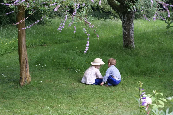 Children sitting under a tree in a garden — Stock Photo, Image