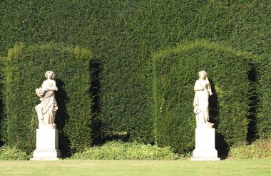 Statues of women. women statues in front of a hedge clipart