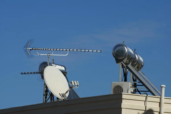 Solar water heating, satellite dish, and a TV aerial on a roof of a house — Stock Photo, Image