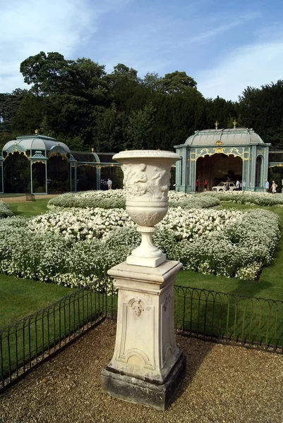 Urne sculptée sur un socle devant un jardin & une volière — Photo