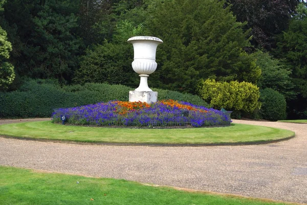 Urn on a plinth and a flower bed — Stock Photo, Image