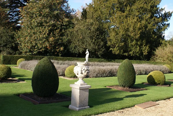 Urna esculpida em um plinto e uma estátua em um jardim topiário — Fotografia de Stock