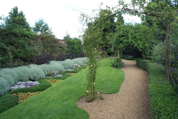 Camino de jardín con un parterre, arco de rosa, césped y seto — Foto de Stock