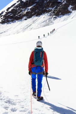 İp ekibi, buzul üzerinde kramponlarla Sexegertenferner 'a doğru Sexegertenspitze ve Avusturya' nın Tyrol Alps şehrinde mavi gökyüzü ile dağ kar panoramasına tırmanıyor.