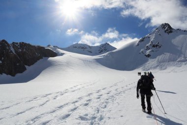 Halat ekibi buzul Taschachferner üzerindeki kramponlarla dağcılık yapıyor Wildspitze 'ye doğru ve Avusturya' nın Tyrol Alps şehrinde mavi gökyüzü olan dağ kar panoramasına doğru.