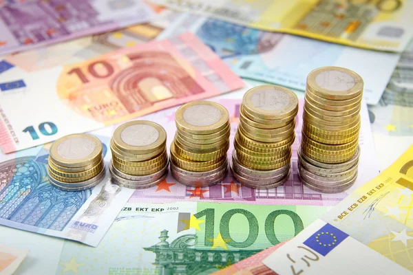 Aumento de las pilas de monedas en euros en billetes en euros — Foto de Stock