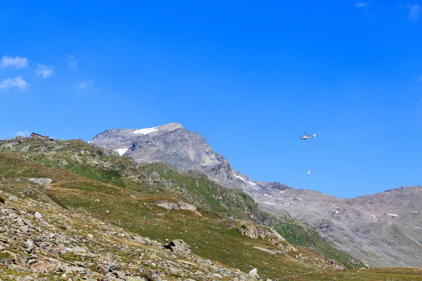 Helicóptero de transporte que vuela con suministros y panorama de montaña con cabaña alpina en Hohe Tauern Alps, Austria —  Fotos de Stock