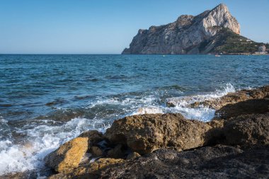 Deniz dalgaları, arka planda Calpe kayalığı, Alicante, İspanya ile birlikte kayalık kıyı şeridine doğru kırılıyor.