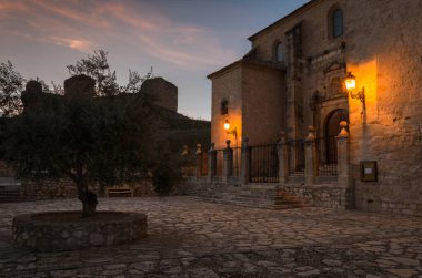 Gün batımında Cogolludo Kilisesi 'nin ışıklandırılmış sokak lambaları ve arka planda şato, Guadalajara, İspanya
