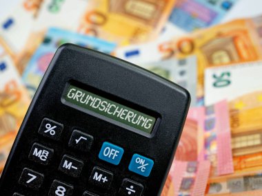 Banknotların önündeki ekranda Grundsicherung sözcüğünün olduğu cep hesap makinesi