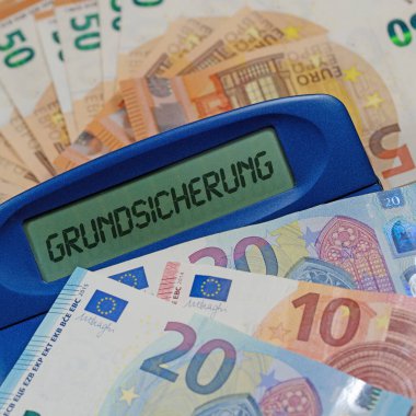 Banknotların önündeki ekranda Grundsicherung sözcüğünün olduğu cep hesap makinesi