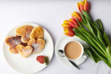 Beyaz bir tabakta, kalp şeklinde peynirli kekler üzerine çilek serpiştirilmiş şeker serpiştirilmiş. 