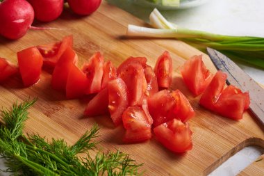 Tahtanın üzerinde kırmızı bir domates ve doğranmış dereotu var.