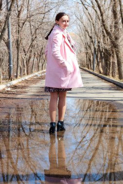 Ağaçların yansımasıyla su birikintisinde yürüyen bir kadın.