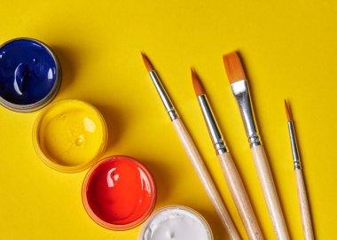 Sarı arka planda renkli guaj ve fırçalar duruyor