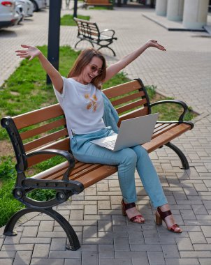 Bankta dizüstü bilgisayarlı neşeli bir kadın oturuyor.