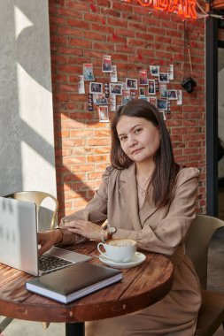 Bir kafede, bir masada, kahverengi elbiseli bir kız çalışıyor.