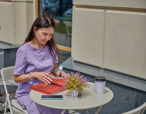 Chica en un vestido con un libro en un café se sienta — Foto de Stock