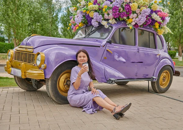 A woman is sitting by the lilac car on the sidewalk — Stock Photo, Image