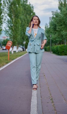 Telefonu olan bir kız kaldırımda yürüyor.