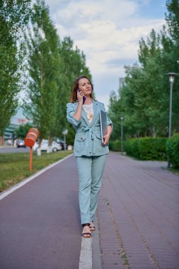 Kaldırımda elinde telefonla yürüyen bir kadın var.