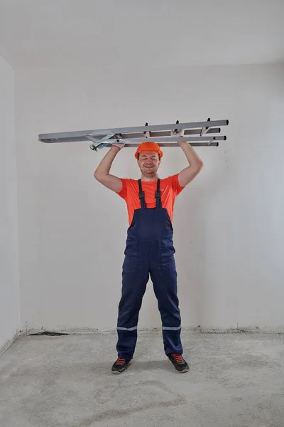 Un trabajador en un casco está de pie con una escalera —  Fotos de Stock