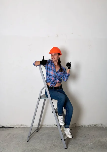 Gaie fille dans un casque se trouve sur un escabeau — Photo