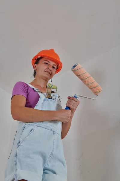 Строитель в комбинезоне держит в руках ролик с краской — стоковое фото