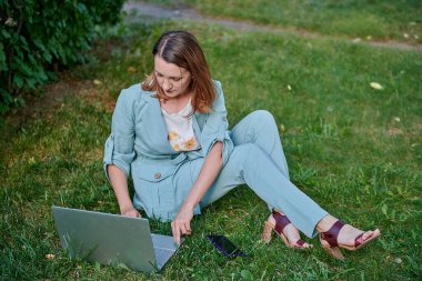 Güzel kız çimlerin üzerinde dizüstü bilgisayarla çalışıyor.
