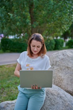 Tatmin olmuş bir kız elinde bilgisayarla çakıl taşının üzerinde oturuyor.