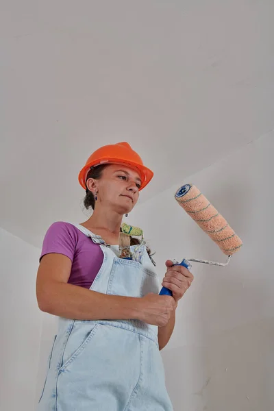 Dans un casque dur un constructeur en salopette tient un rouleau de peinture — Photo