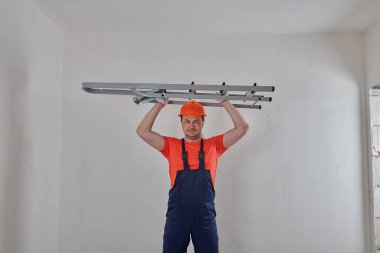 Turuncu kasklı bir inşaatçının elinde merdiven vardır.