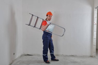 Ciddi bir mühendis kolunun altında merdiven tutuyor.
