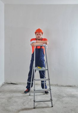 Miğferli bir inşaat işçisi merdivene yaslanmış.