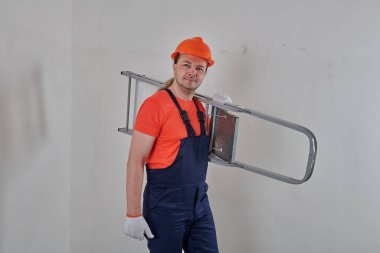 Mavi tulumlu bir işçi merdiven tutar.