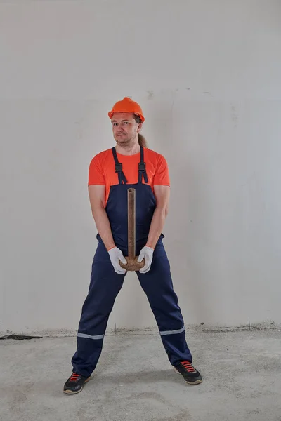 In overalls een man met een moker in zijn handen in een helm — Stockfoto